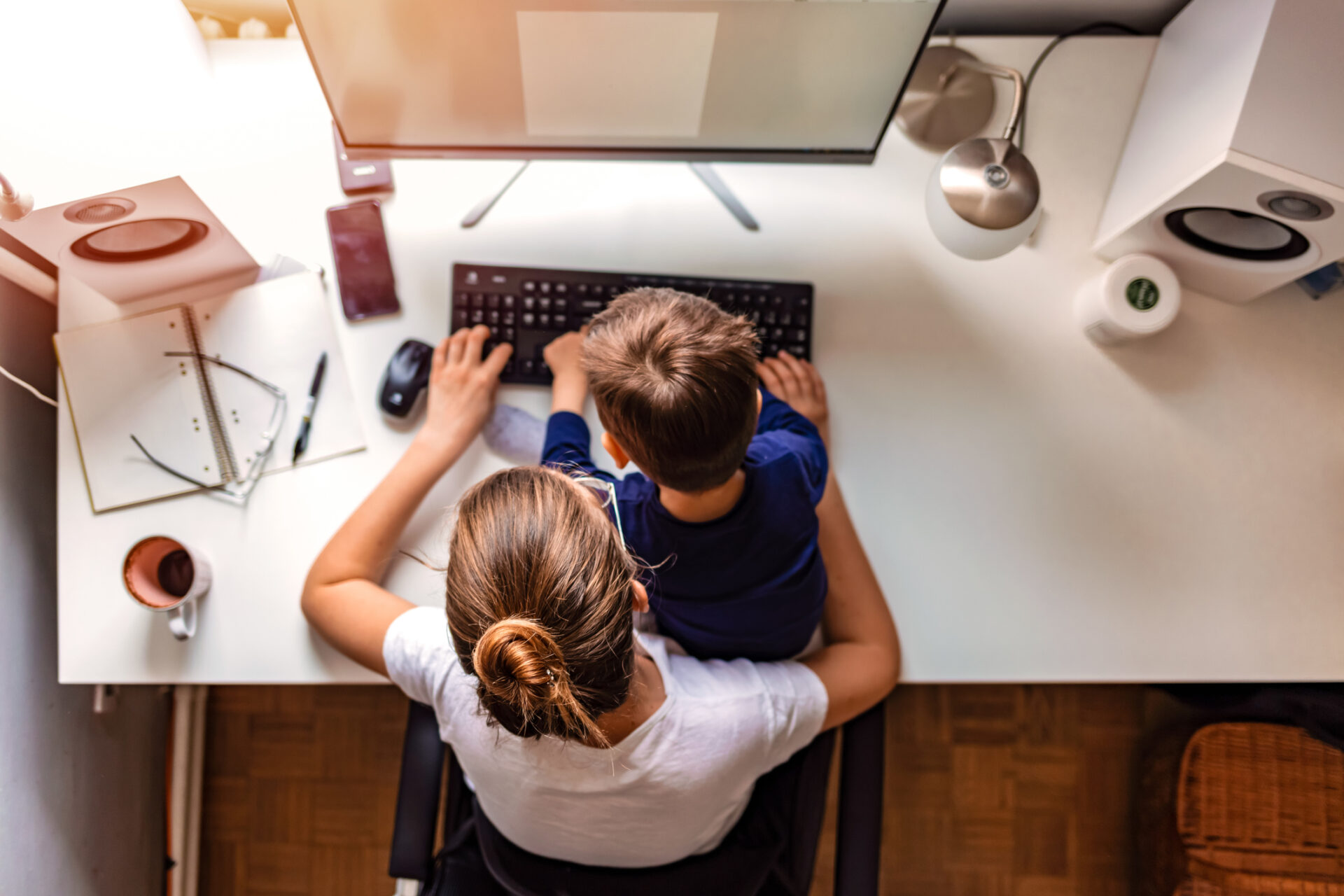 Overhead view of young mother working on computer with her son sitting in her lap during the day.